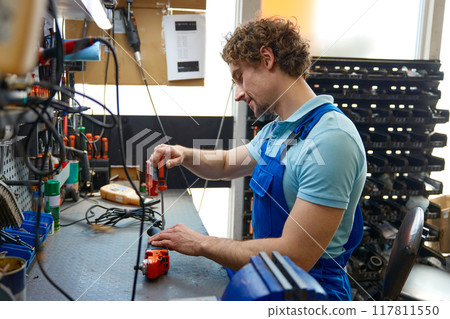 Professional repairman fixing angle grinder power tool at workshop 117811550