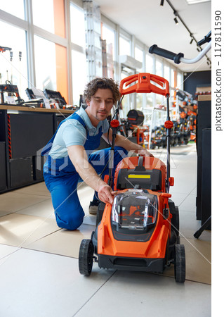 Worker customer choosing electric lawnmower at garden supply store 117811590