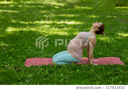 Pregnant caucasian woman doing yoga in the park. Back bend. Pregnant caucasian woman doing yoga in the park. Back bend. 117811632