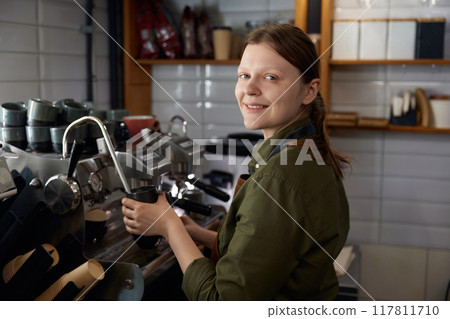 Portrait of woman barista cooking cappuccino on coffeemaker machine 117811710