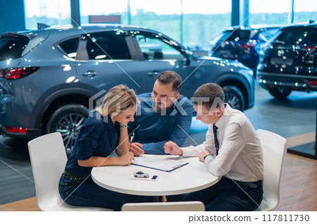 Happy caucasian couple signs a contract for the purchase of a car salon. Happy caucasian couple signs a contract for the purchase of a car salon. 117811730
