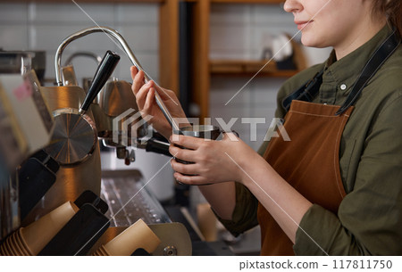 Closeup cropped shot of barista preparing latte with milk foam on coffee machine 117811750