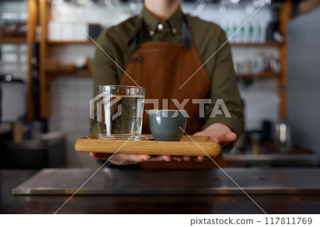 Closeup glass of water and coffee cup on wooden tray in female barista hands 117811769