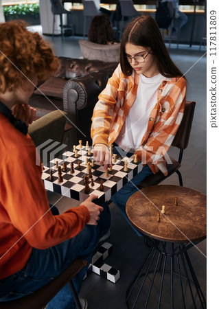 Boy and girl playing chess in modern studio 117811809