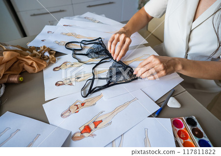 Faceless woman draws underwear sketches. Close-up of fashion designer's hands with lace bra. Faceless woman draws underwear sketches. Close-up of fashion designer's hands with lace bra. 117811822