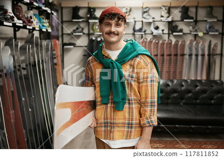 Portrait of man carrying snowboards equipment over sports shop background 117811852