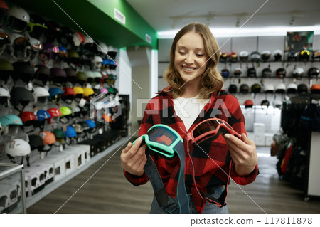 Young smiling woman choosing protective eye goggles mask at sports shop 117811878