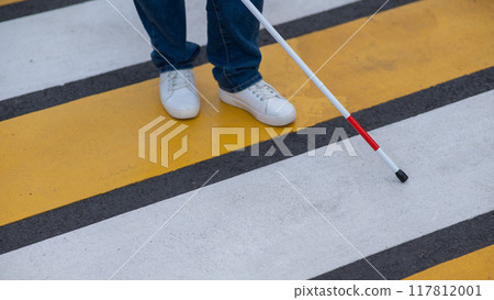 Close-up of the legs of a blind woman crossing the road at a crosswalk with a cane. Close-up of the legs of a blind woman crossing the road at a crosswalk with a cane. 117812001