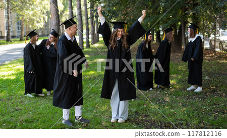 A group of graduates in robes congratulate each other on their graduation outdoors. A group of graduates in robes congratulate each other on their graduation outdoors. 117812116