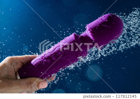 A woman washes a purple vibrator under the shower. Waterproof sex toy on a blue background. A woman washes a purple vibrator under the shower. Waterproof sex toy on a blue background. 117812145