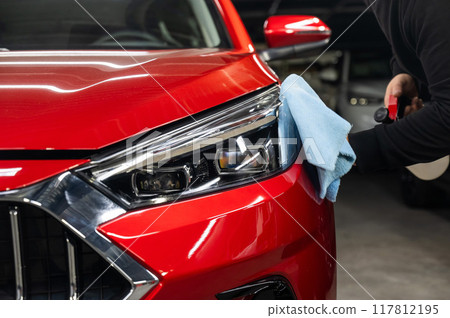 A man washes the headlights of a red car using a microfiber cloth and spray. A man washes the headlights of a red car using a microfiber cloth and spray. 117812195