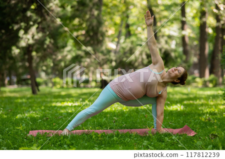 Pregnant caucasian woman doing yoga in the park. Pregnant caucasian woman doing yoga in the park. 117812239