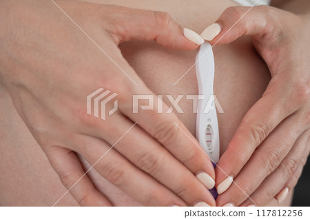 Caucasian woman holding a positive express pregnancy test against the background of her tummy. Caucasian woman holding a positive express pregnancy test against the background of her tummy. 117812256