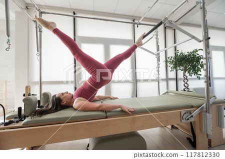 Woman doing pilates exercise on cadillac reformer machine.  117812330