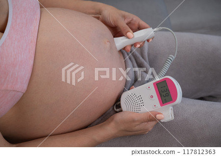 Close-up of a pregnant woman's belly using a home doppler. Normal baby heartbeat. 117812363