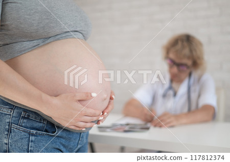 Doctor obstetrician gynecologist at his desk in the background. Close-up of a pregnant woman's belly. 117812374