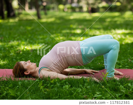 Pregnant caucasian woman doing yoga in the park. Prenatal shoulder bridge exercise. Pregnant caucasian woman doing yoga in the park. Prenatal shoulder bridge exercise. 117812381