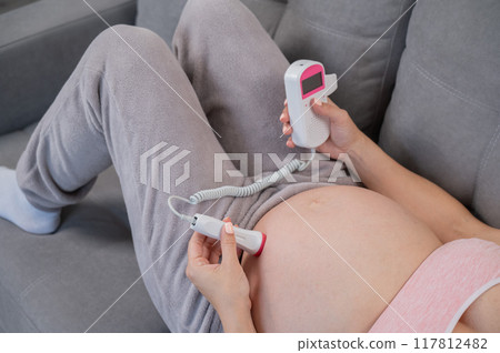 Close-up of a pregnant woman's belly using a home doppler. Blank screen. Close-up of a pregnant woman's belly using a home doppler. Blank screen. 117812482