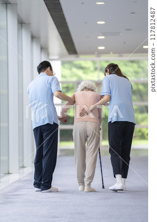 護理人員支持一名拄著拐杖行走的老年婦女，後視 117812487