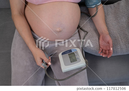 Close-up of the belly of a pregnant woman measuring blood pressure with a tonometer. Hypotension. Close-up of the belly of a pregnant woman measuring blood pressure with a tonometer. Hypotension. 117812506