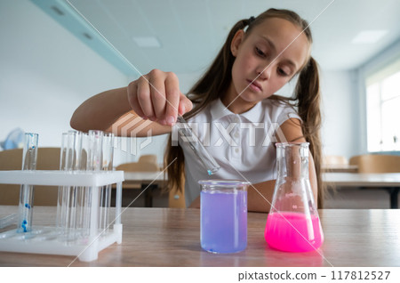 A schoolgirl conducts experiments in a chemistry lesson. Girl pouring colored liquids from a beaker. A schoolgirl conducts experiments in a chemistry lesson. Girl pouring colored liquids from a beaker. 117812527