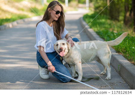 Blind young woman cuddling with guide dog on a walk outdoors.  117812634