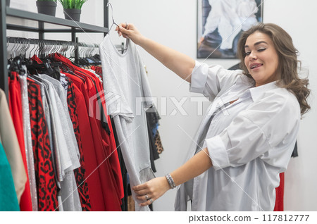 A fat woman chooses clothes in a plus size store.  117812777