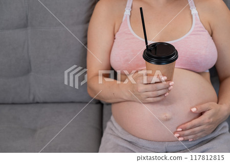 Faceless pregnant woman in 3rd trimester holding a coffee glass on her belly. Faceless pregnant woman in 3rd trimester holding a coffee glass on her belly. 117812815