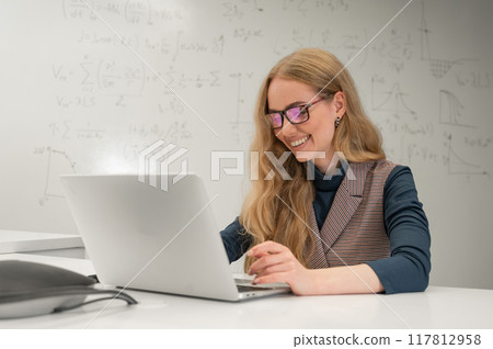 Caucasian woman scientist typing on laptop. White board with formulas. Caucasian woman scientist typing on laptop. White board with formulas. 117812958