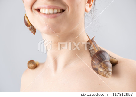Close-up portrait of a Caucasian woman with snails on her face. The use of shellfish in cosmetology. 117812998