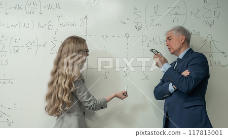 Female student answers a question from an elderly professor at a white board. Female student answers a question from an elderly professor at a white board. 117813001