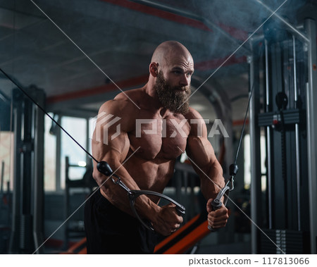 Bald Caucasian bodybuilder training chest using cable crossover in gym.  117813066
