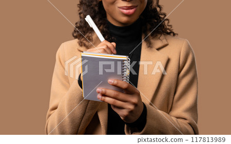 African teen girl writing notes in planner with pen. Woman thinking about future African teen girl writing notes in planner with pen. Woman thinking about future 117813989