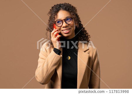 Attractive african woman talking by phone, smiling. Young student lady on beige 117813998