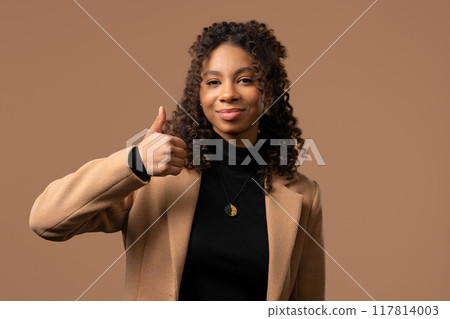Positive woman with hand sign like, thumbs up gesture. Lady on beige background Positive woman with hand sign like, thumbs up gesture. Lady on beige background 117814003