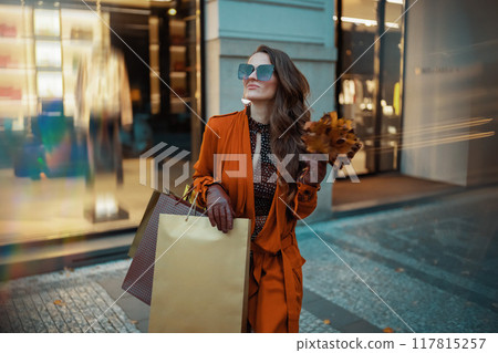 modern woman in orange trench coat with shopping bags 117815257