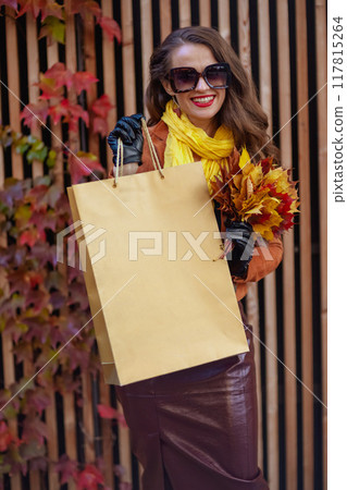 happy young woman in brown trench coat with shopping bag 117815264