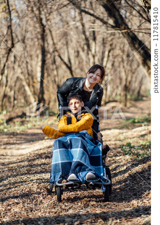 Mother and child with special needs enjoying nature walk in forest, accessibility in outdoor activities, disability inclusion, family bonding, adaptive equipment. Mother and child with special needs enjoying nature walk in forest, accessibility in outdoor activities, disability inclusion, family bonding, adaptive equipment. 117815410