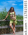 Summer elegance: Young woman in a green bikini on a wooden walkway 117815855
