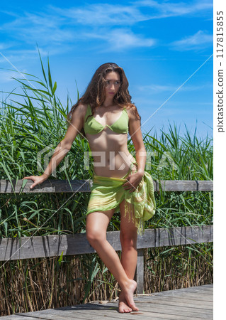 Summer elegance: Young woman in a green bikini on a wooden walkway 117815855