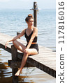 Relaxed summer atmosphere at the lake: woman in a black lace outfit on a jetty 117816016