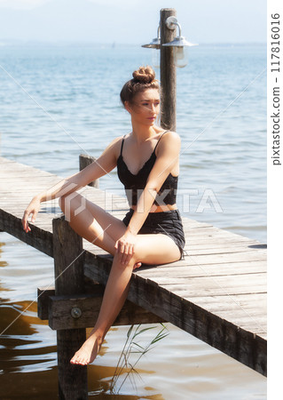 Relaxed summer atmosphere at the lake: woman in a black lace outfit on a jetty Relaxed summer atmosphere at the lake: woman in a black lace outfit on a jetty 117816016