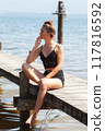 Thoughtful pause by the lake: woman in a black lace outfit on a jetty 117816592