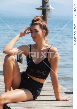 Sun-kissed: Woman in a black lace top enjoys the summer breeze by the lake 117816594