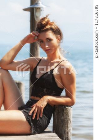 Elegance by the water: woman in a black lace outfit on a jetty by the lake Elegance by the water: woman in a black lace outfit on a jetty by the lake 117816595