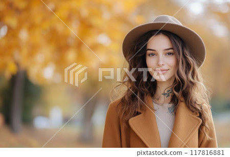 Young woman with curly hair poses in a cozy outfit during autumn in a park 117816881