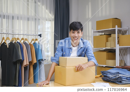 Portrait of a confident young online entrepreneur working from his home office, surrounded by clothing products and shipping boxes. 117816964