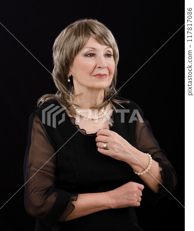 Mature Woman in Blonde Wig and Dark Dress Wears Imitation Pearl Jewelry, Embodying Classic Elegance and Timeless Beauty Against Black Backdrop. 117817086