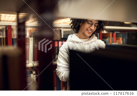 Smiling university student reading books in library Smiling university student reading books in library 117817616