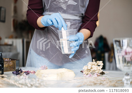 Close-up of hands mixing resin for DIY art project, wearing blue gloves and apron. Creative hobby, craft, eco-friendly home decor, handmade, sustainability. Close-up of hands mixing resin for DIY art project, wearing blue gloves and apron. Creative hobby, craft, eco-friendly home decor, handmade, sustainability. 117818093